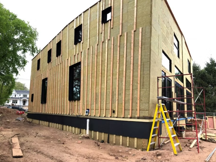 A large modern building under construction showing the installation of Rockwool insulation panels for an External Thermal Insulation Composite System (ETICS)
