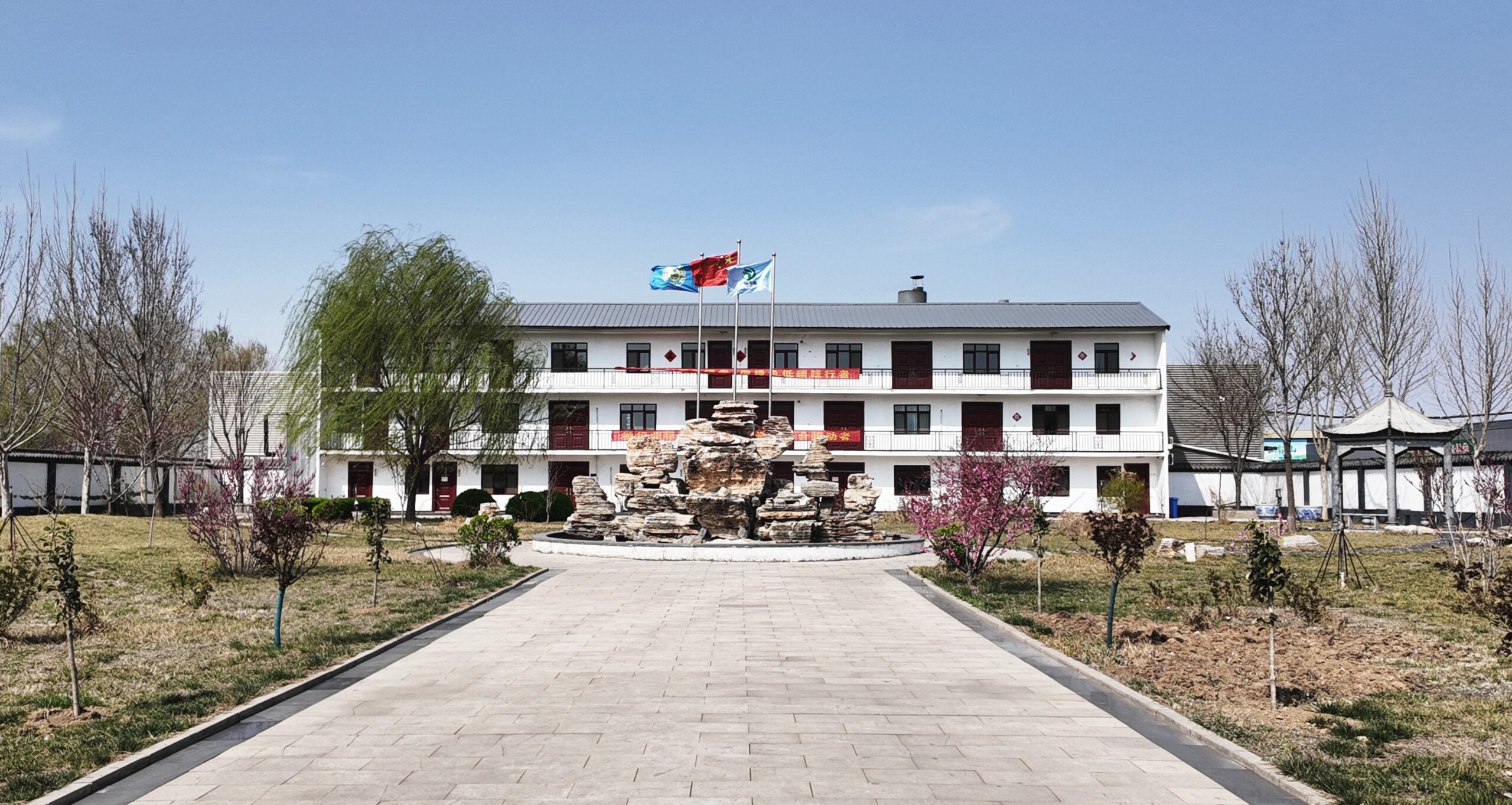 Authentic view of RSINSULATIONBOARD headquarters in Hebei featuring corporate building, ornamental rockery, and flags under clear blue sky